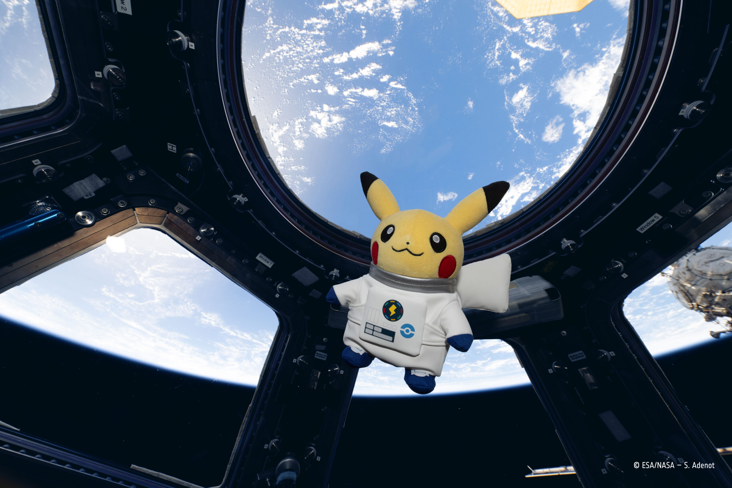 国際宇宙ステーション(ISS)のキューポラ(展望窓)で、宇宙服姿のピカチュウのぬいぐるみが地球を背景に浮かんでいる