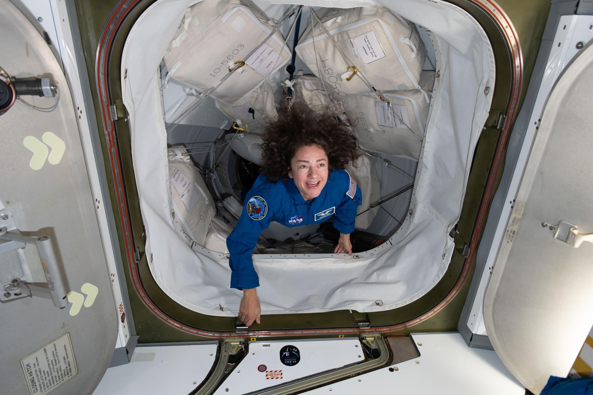 ドラゴン宇宙船とのドッキング後、ハッチを通って国際宇宙ステーションに入る青い飛行服のジェシカ・メイア宇宙飛行士