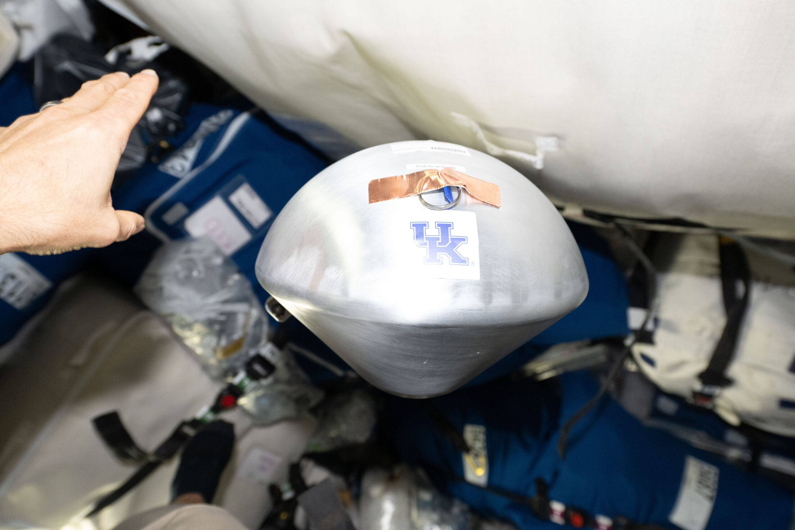 シグナスXL貨物船の船内で宙に浮かぶ、ケンタッキー大学のロゴが付いた銀色のKREPE-3カプセル
