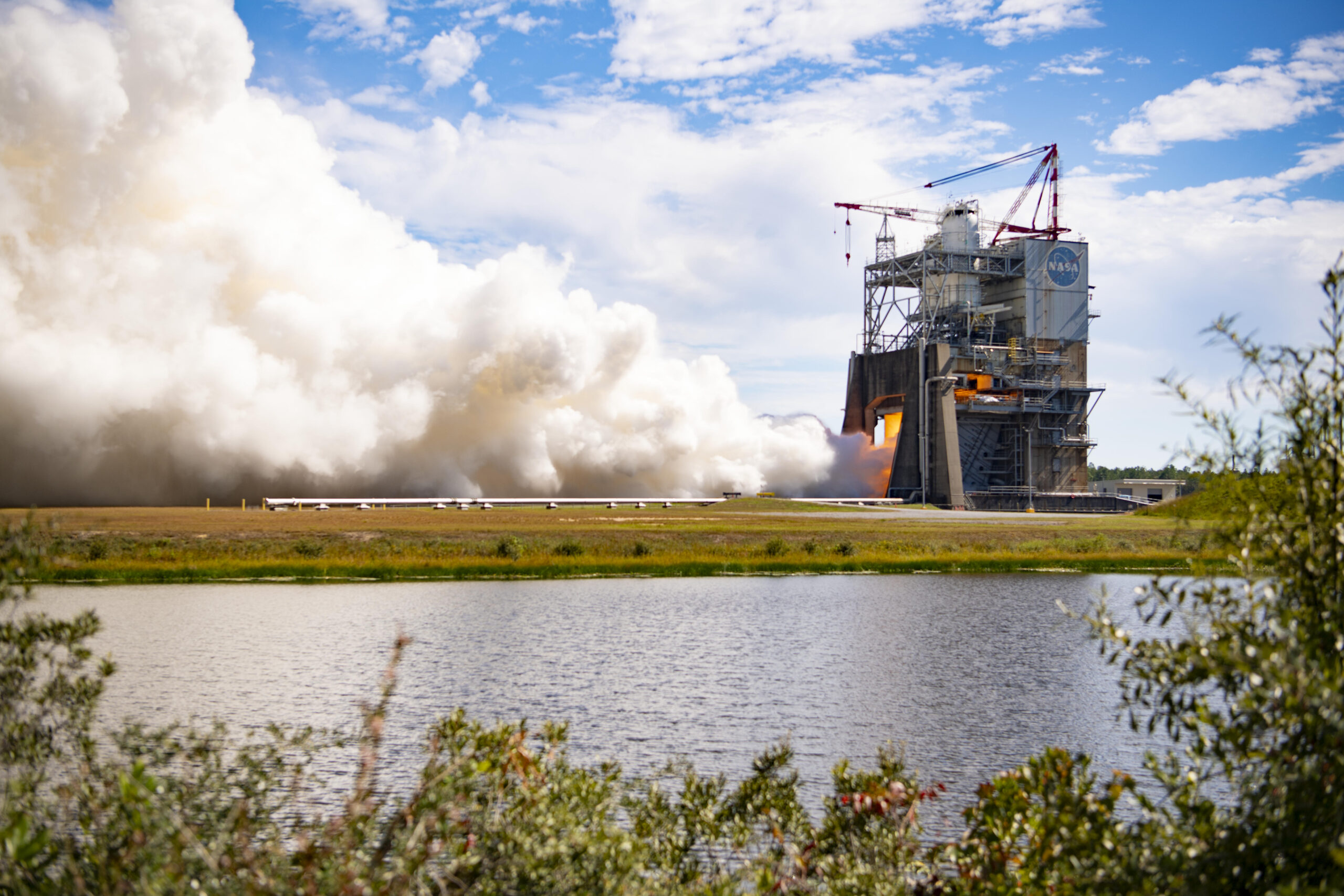 スティニス宇宙センターの試験スタンドで燃焼中のRS-25エンジンと、左に広がる白い排気の雲