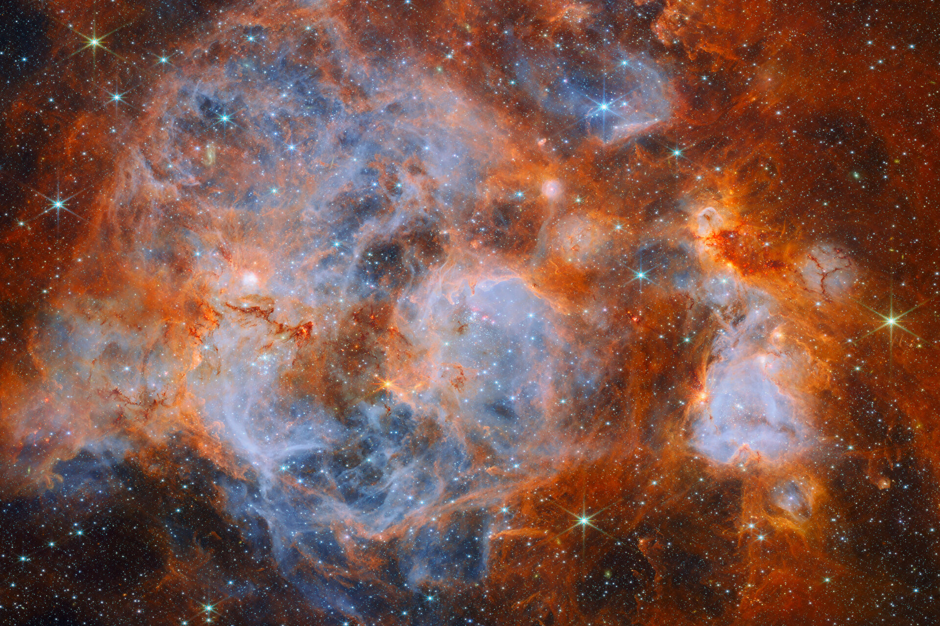 ウェッブが撮影した大マゼラン雲の星形成領域N159。オレンジ色の雲と青いガスが広がる